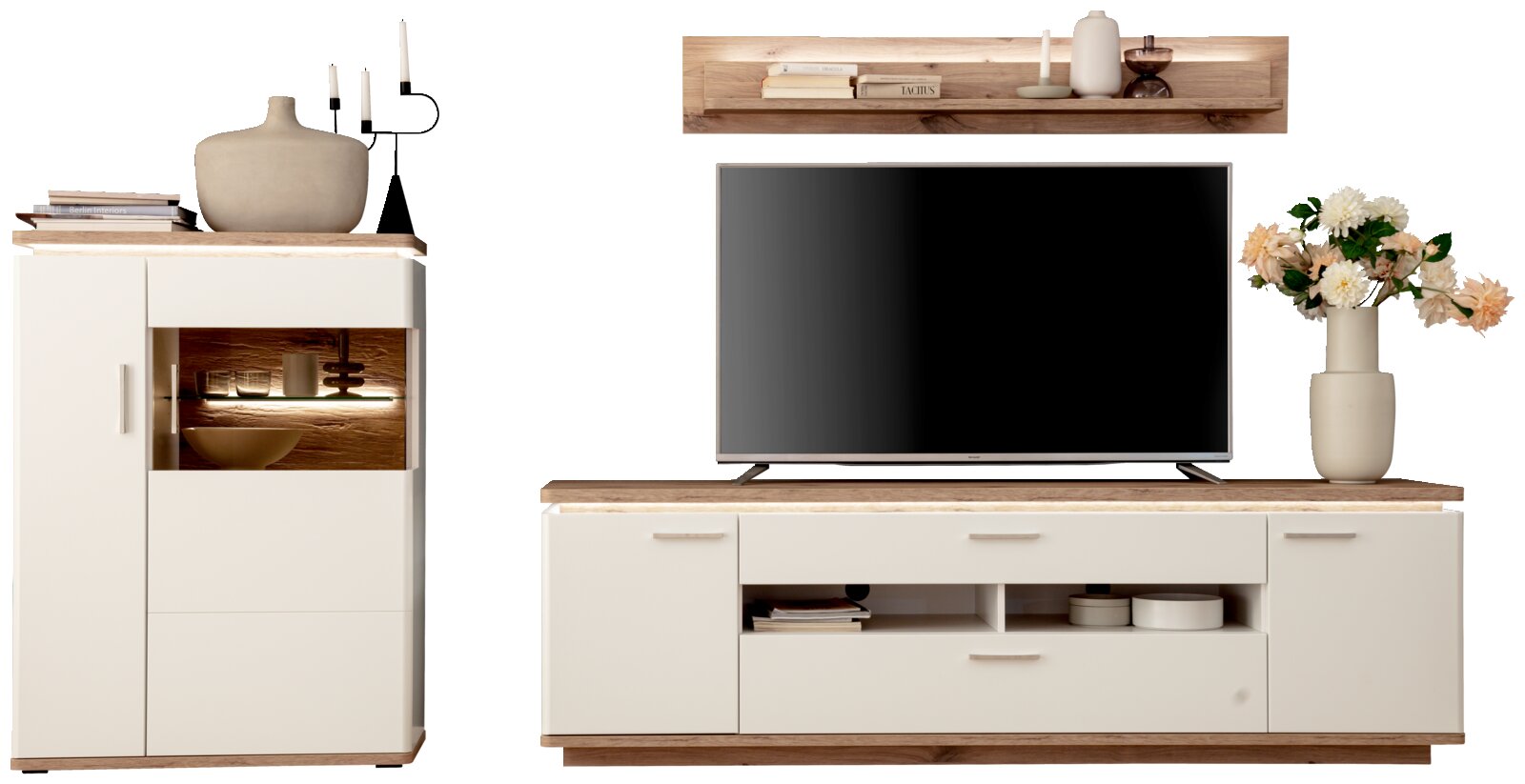 Wohnwand-Set im modernen Design mit TV-Lowboard und Highboard in Weiß mit Holzoptik-Absetzungen, frontal aus der Vorderansicht; auf dem Lowboard steht ein Fernseher, darüber ein Wandregal, dekoriert mit Vase, Kerzen und Blumen.