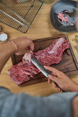 Fleischmesser schneidet rohes Fleisch auf einem Holzbrett, von oben betrachtet.