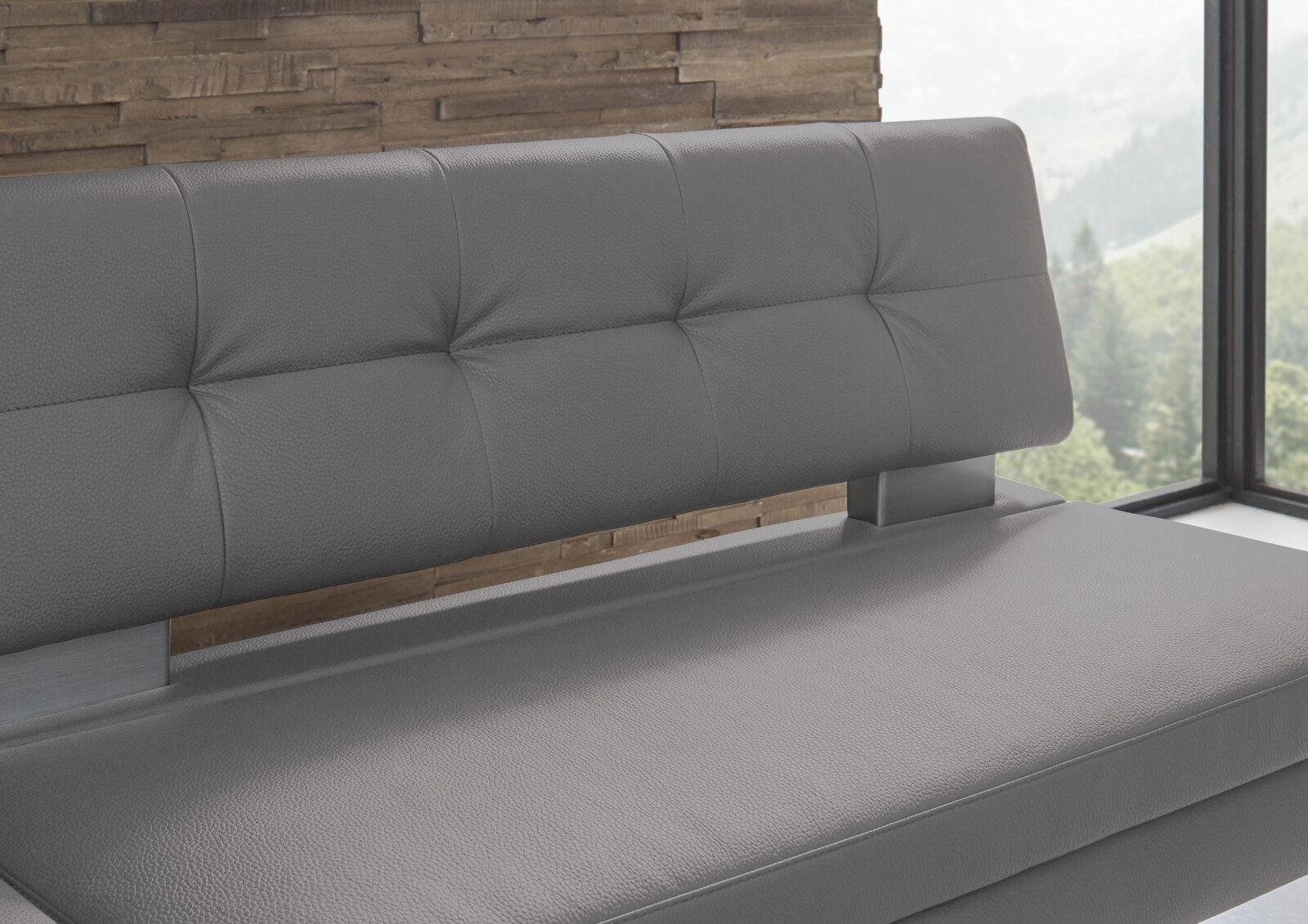 Graue Eckbank mit gepolsterter Rückenlehne und Sitzfläche, seitliche Perspektive vor einer Holzwand und Fenster mit Blick ins Grüne.