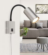 Moderne Wandleuchte aus mattem Nickel mit flexiblem Arm, seitliche Perspektive, montiert an einer weißen Wand in einem stilvollen Wohnzimmer.