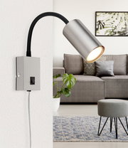 Moderne Wandleuchte aus mattem Nickel mit flexiblem Arm, seitliche Perspektive, montiert an einer weißen Wand in einem stilvollen Wohnzimmer.