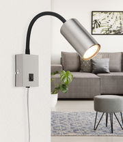 Moderne Wandleuchte aus mattem Nickel mit flexiblem Arm, seitliche Perspektive, montiert an einer weißen Wand in einem stilvollen Wohnzimmer.