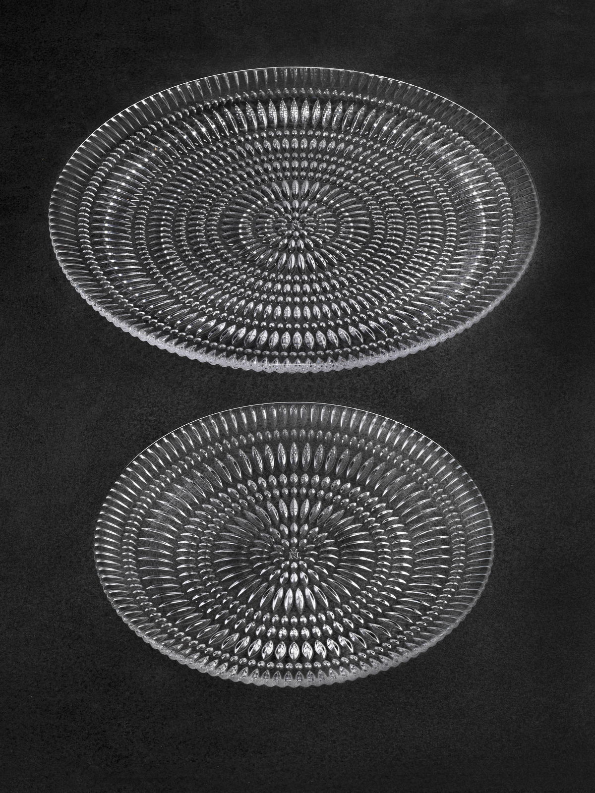 Zwei gläserne Teller mit einem detaillierten, ethnischen Muster, von oben betrachtet.