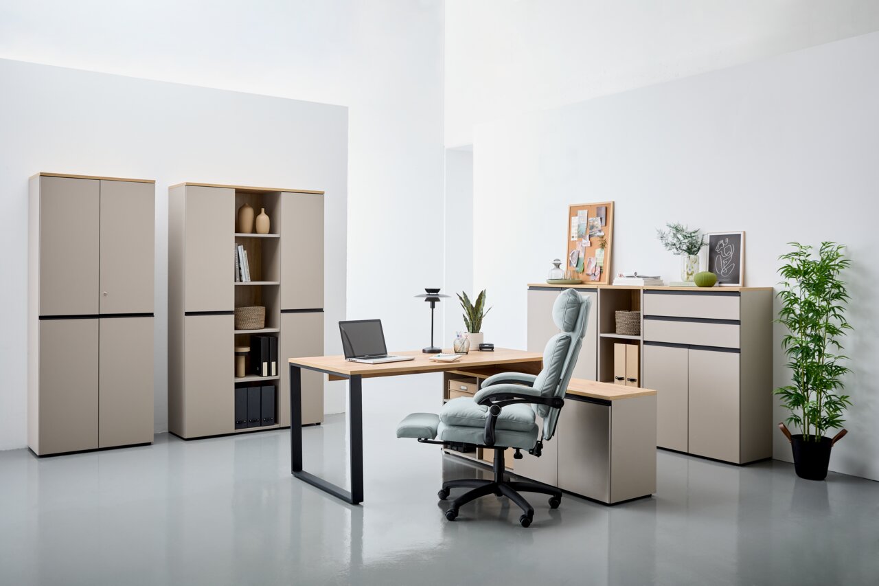 Novel Winkelschreibtisch DELTONA Moderne Büromöbel in einem hellen Raum, bestehend aus einem Winkelschreibtisch mit Laptop, einem ergonomischen Bürostuhl und mehreren Aktenschränken. Perspektive von vorne.