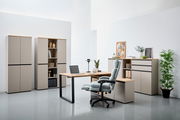 Moderne Büromöbel in einem hellen Raum, bestehend aus einem Winkelschreibtisch mit Laptop, einem ergonomischen Bürostuhl und mehreren Aktenschränken. Perspektive von vorne.