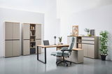 Moderne Büromöbel in einem hellen Raum, bestehend aus einem Winkelschreibtisch mit Laptop, einem ergonomischen Bürostuhl und mehreren Aktenschränken. Perspektive von vorne.