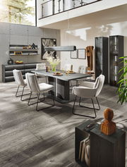 Moderne Esszimmer-Einrichtung mit Esstisch, Stühlen und Vitrinen in einem hellen Raum mit hohen Decken, seitliche Perspektive.