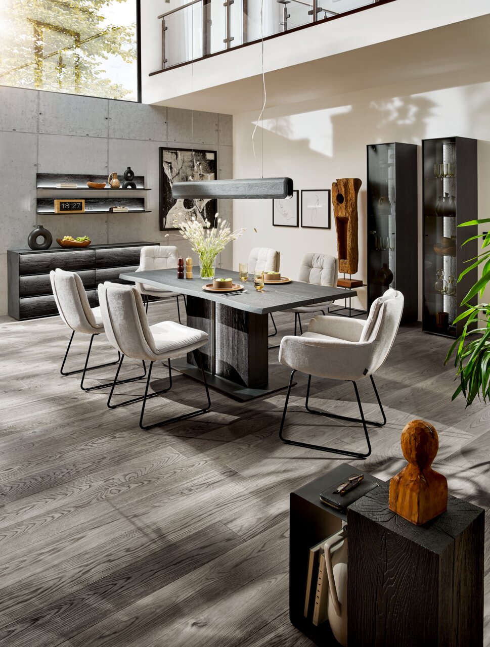 Moderne Esszimmer-Einrichtung mit Esstisch, Stühlen und Vitrinen in einem hellen Raum mit hohen Decken, seitliche Perspektive.