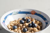Kinderschüssel mit Weltall-Motiv, gefüllt mit Müsli und Blaubeeren, aus seitlicher Perspektive fotografiert.