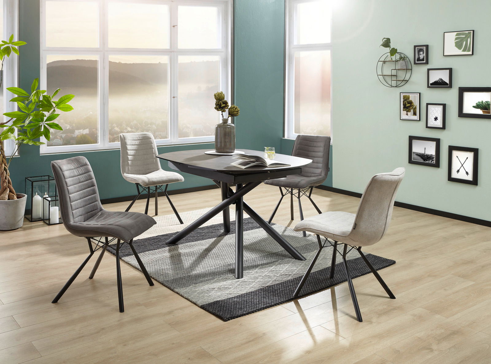 Moderner Esstisch mit schwarzer Tischplatte und gekreuztem Metallgestell, umgeben von vier gepolsterten Stühlen in einem hellen Raum mit großen Fenstern, aus der Perspektive leicht von oben betrachtet.