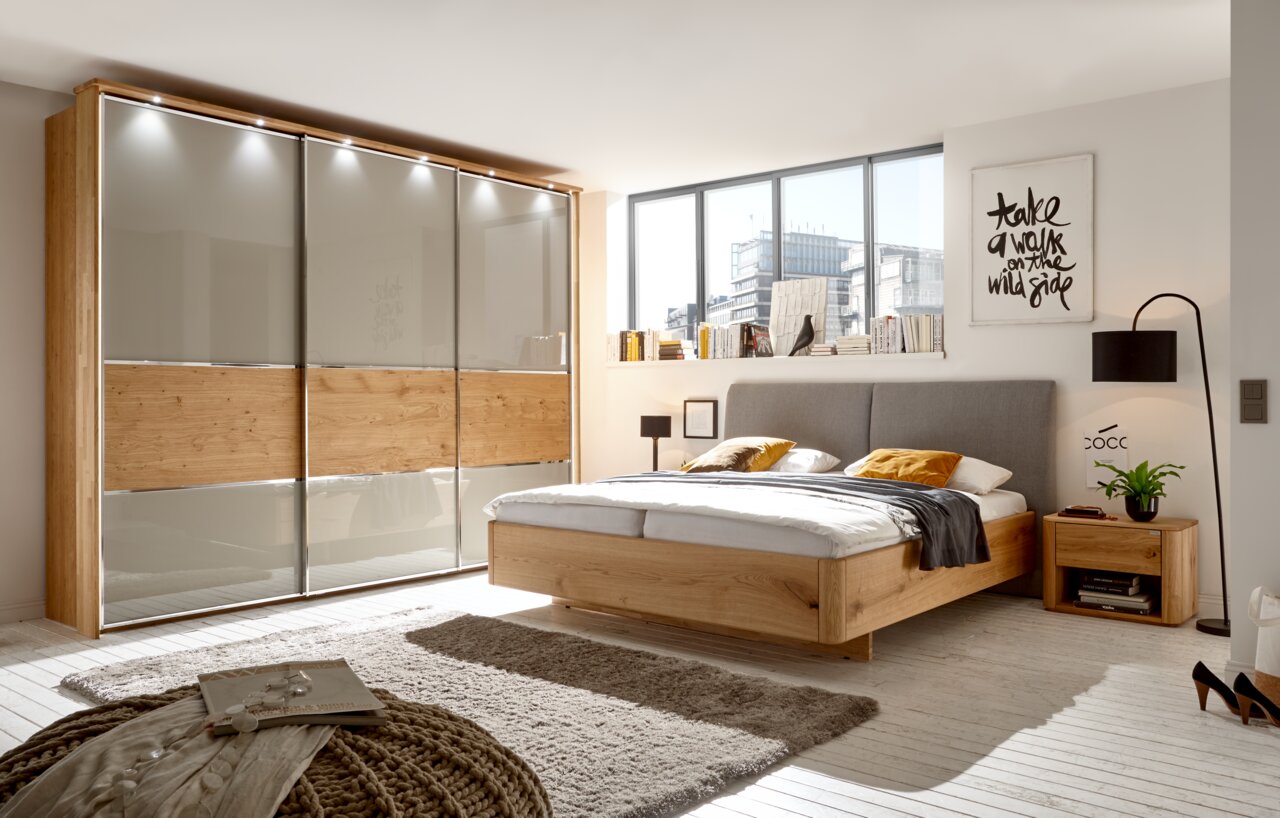 Modernes Schlafzimmer mit Holzbett, grauem Kopfteil und passender Nachtkonsole, seitliche Perspektive