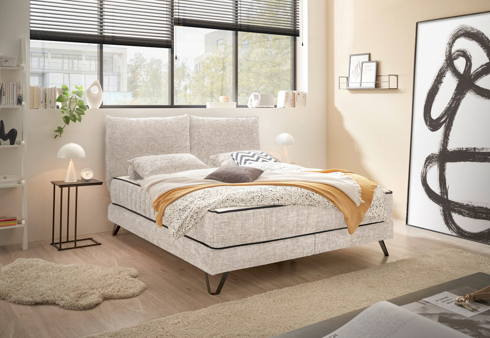 Gemütliches Boxspringbett in einem modernen Schlafzimmer mit großen Fenstern, seitliche Perspektive.