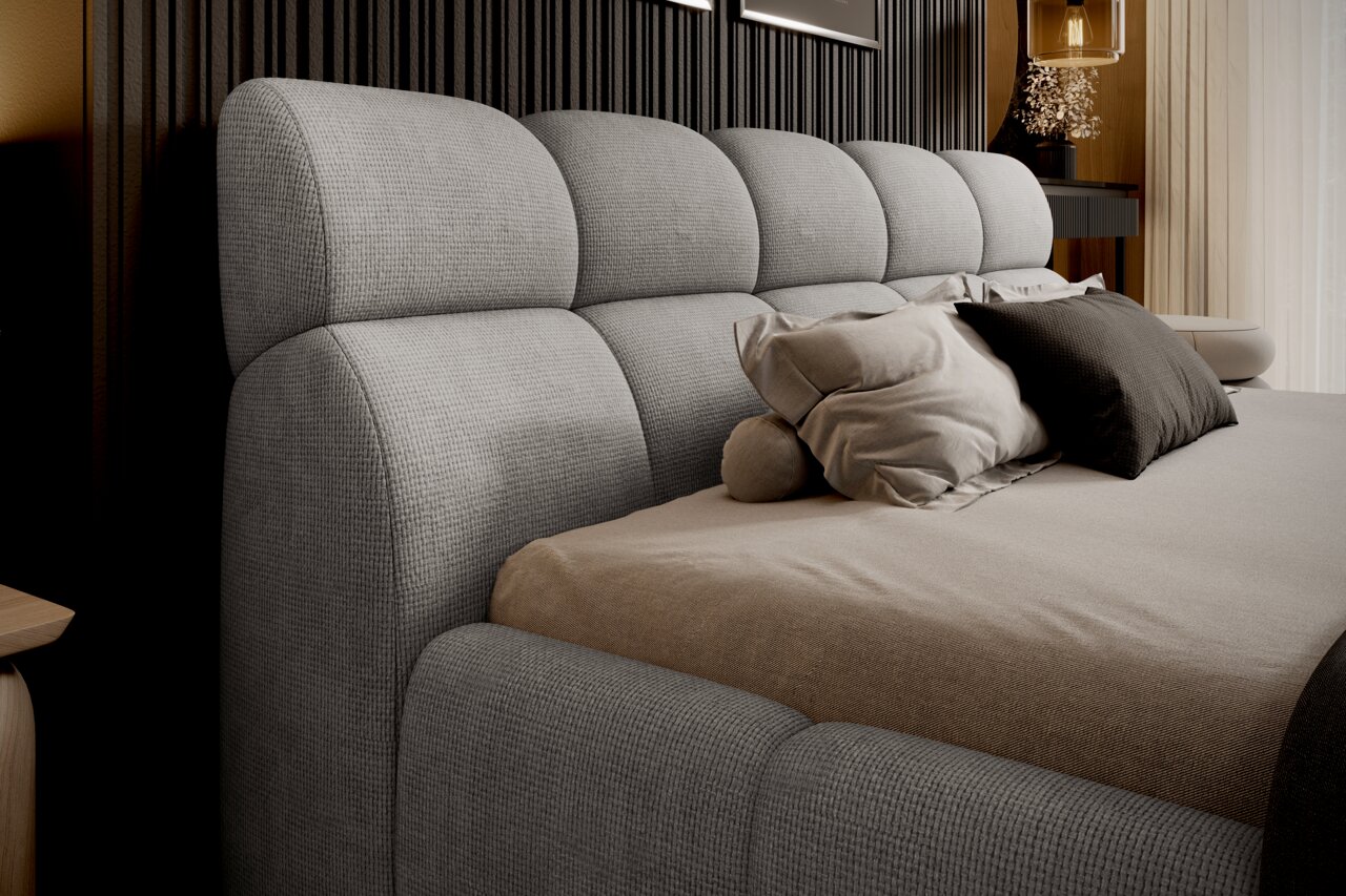 Seitliche Perspektive auf ein graues Polsterbettgestell mit weichem Kopfteil und mehreren Kissen.