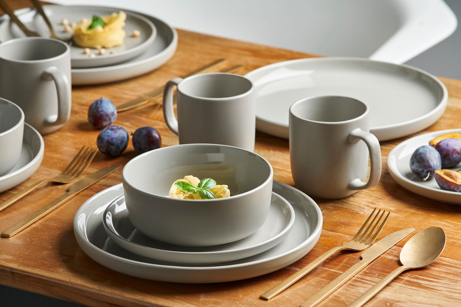 Kombiservice 16-tlg. Linz in moderner, minimalistischer Gestaltung auf einem Holztisch, mit goldfarbenem Besteck und frischen Früchten, aus der Vogelperspektive fotografiert.