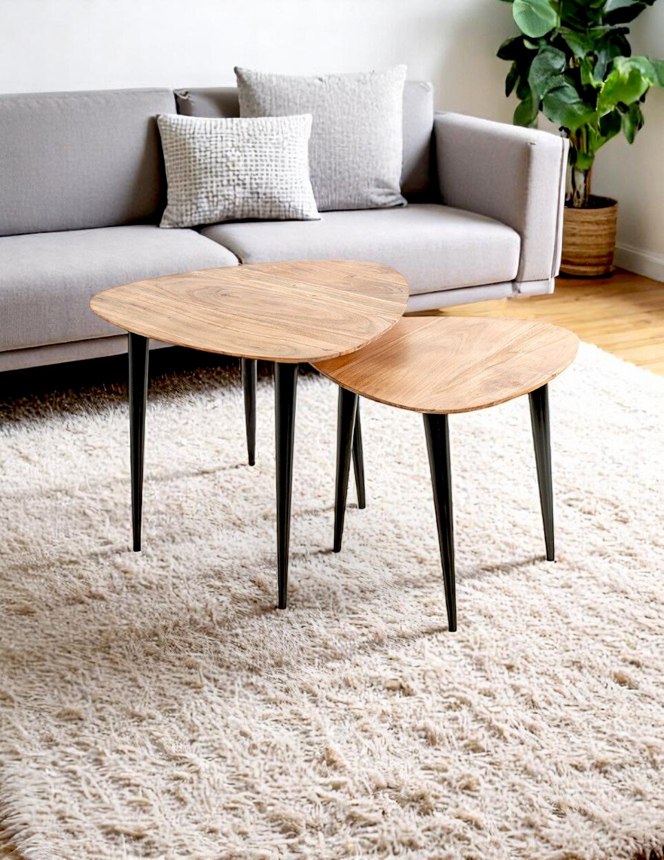 Zwei ineinander schiebbare Couchtische im Set mit dreieckigen Holzplatten und schwarzen Metallbeinen auf hellem Hochflor-Teppich vor grauem Sofa, Perspektive: leicht von oben aus schräger Frontansicht