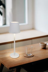 Moderne Akku-Tischleuchte in minimalistischem Design auf einem Holztisch, seitliche Perspektive