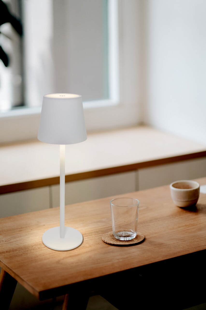 Moderne Akku-Tischleuchte in minimalistischem Design auf einem Holztisch, seitliche Perspektive
