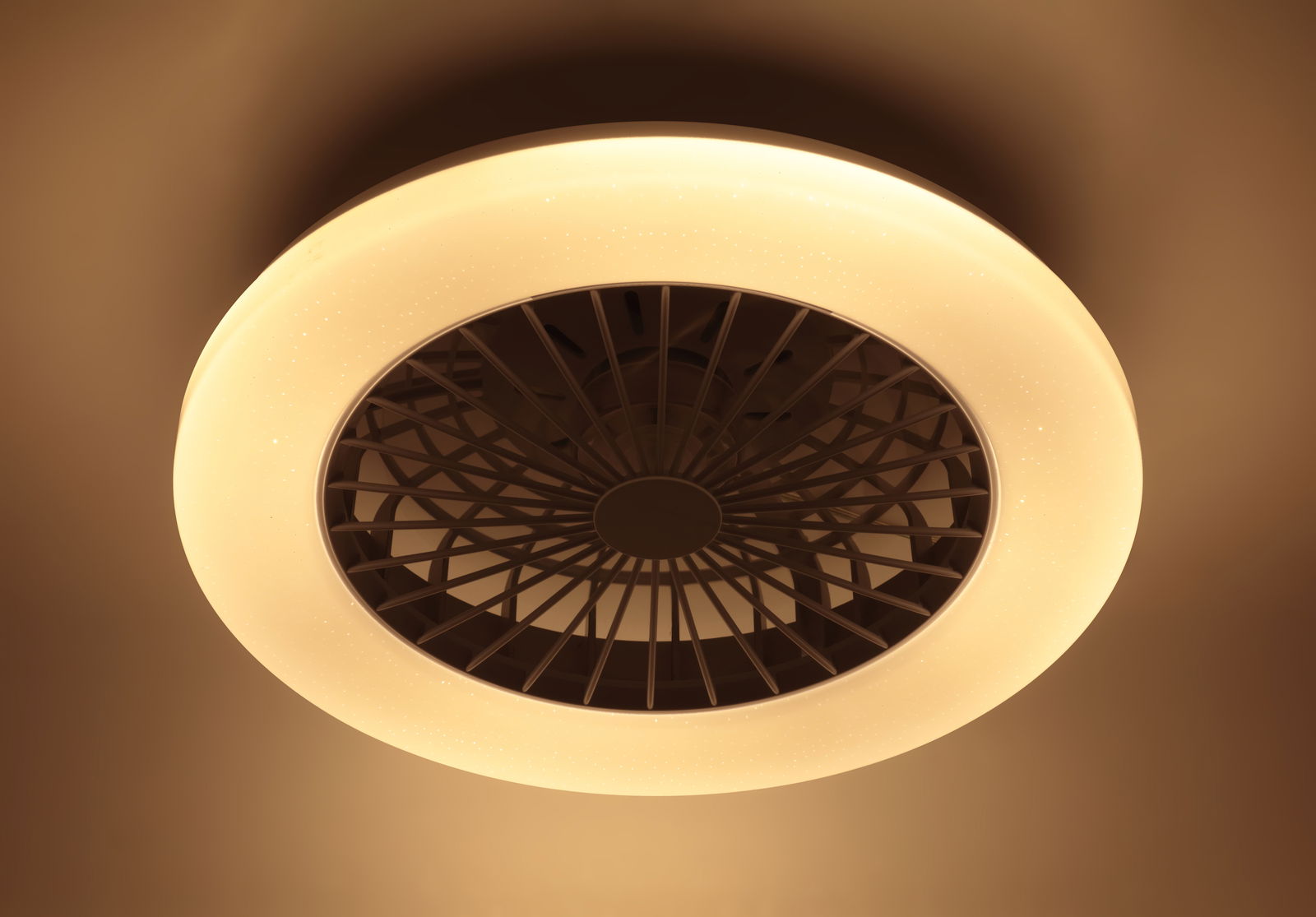 Deckenventilator mit integriertem Licht, von unten betrachtet, in warmem Gelbton leuchtend.