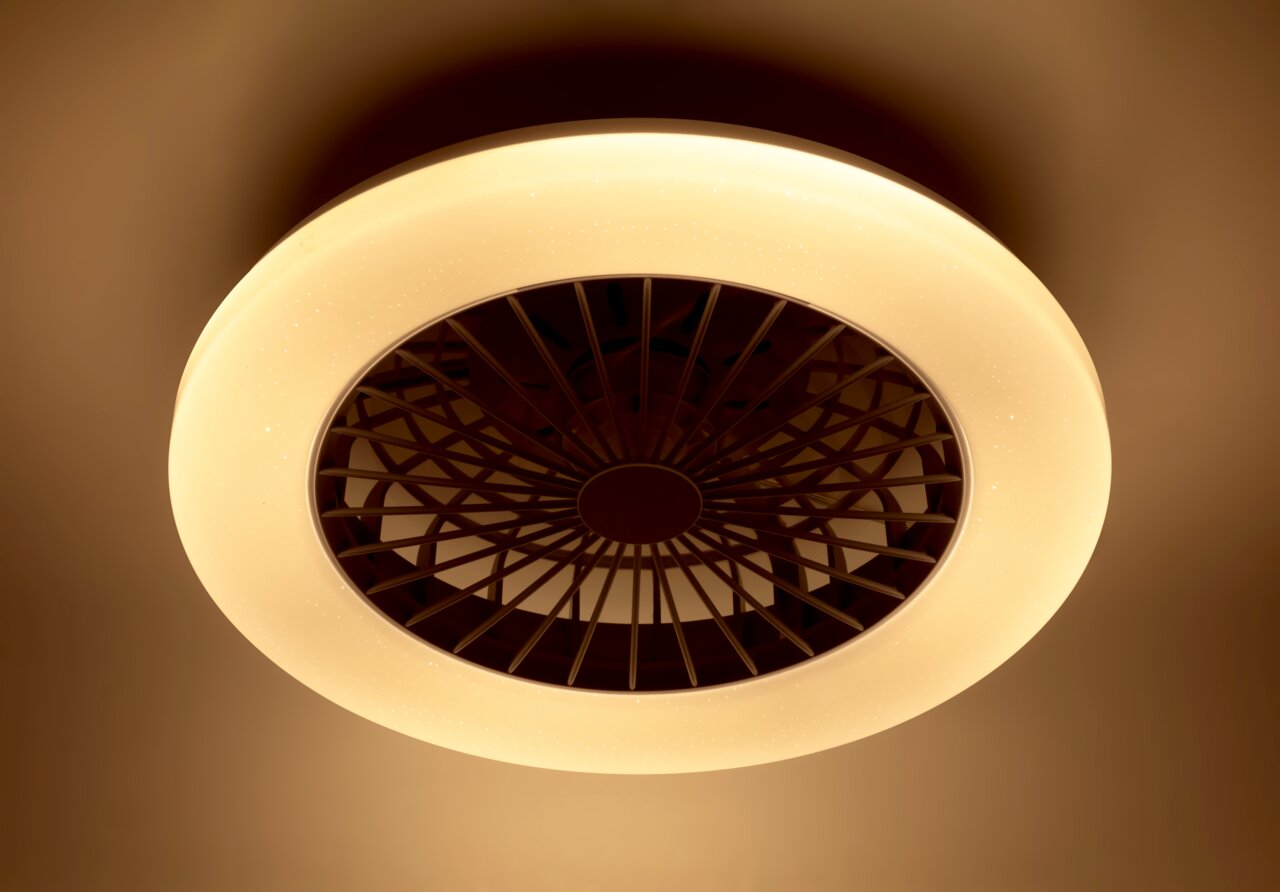 Deckenventilator mit integriertem Licht, von unten betrachtet, in warmem Gelbton leuchtend.