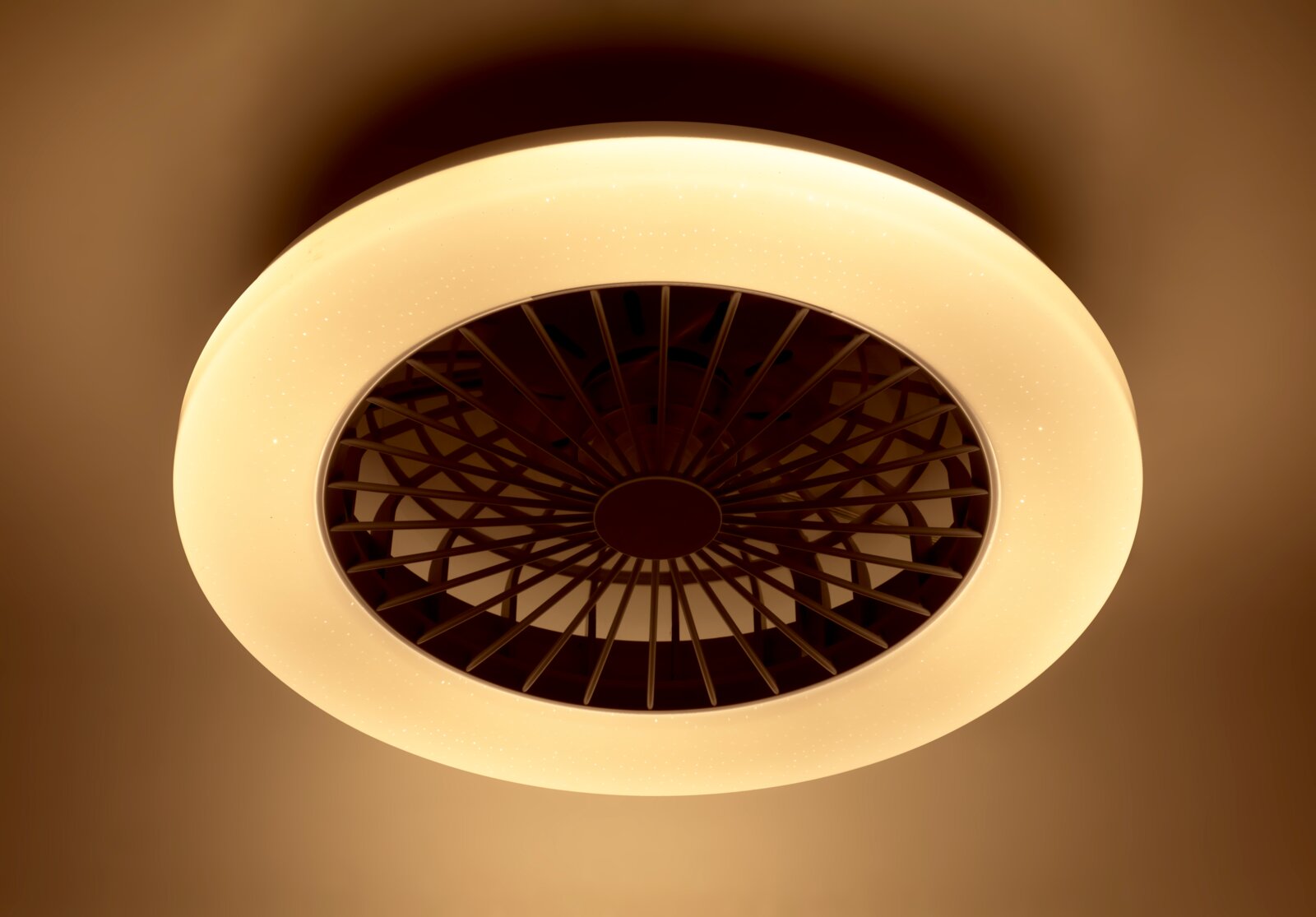 Plafondventilator met ingebouwde verlichting, gezien van onderaf, met een warme gele gloed.