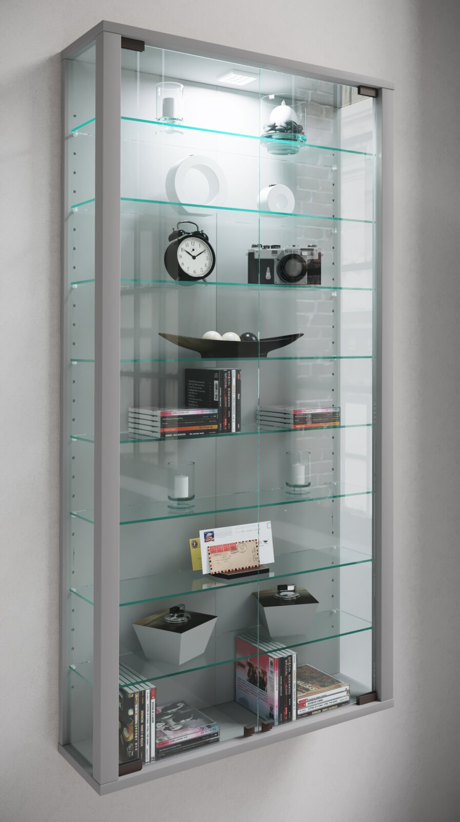 Wandmontierte Glasvitrine mit silbernem Rahmen, LED-Beleuchtung und mehreren Glasböden, bestückt mit Dekoobjekten und Büchern; Perspektive: leicht schräg von vorne links.