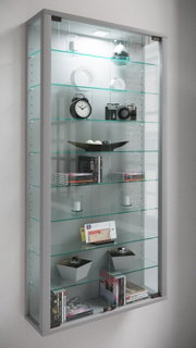Wandmontierte Glasvitrine mit silbernem Rahmen, LED-Beleuchtung und mehreren Glasböden, bestückt mit Dekoobjekten und Büchern; Perspektive: leicht schräg von vorne links.