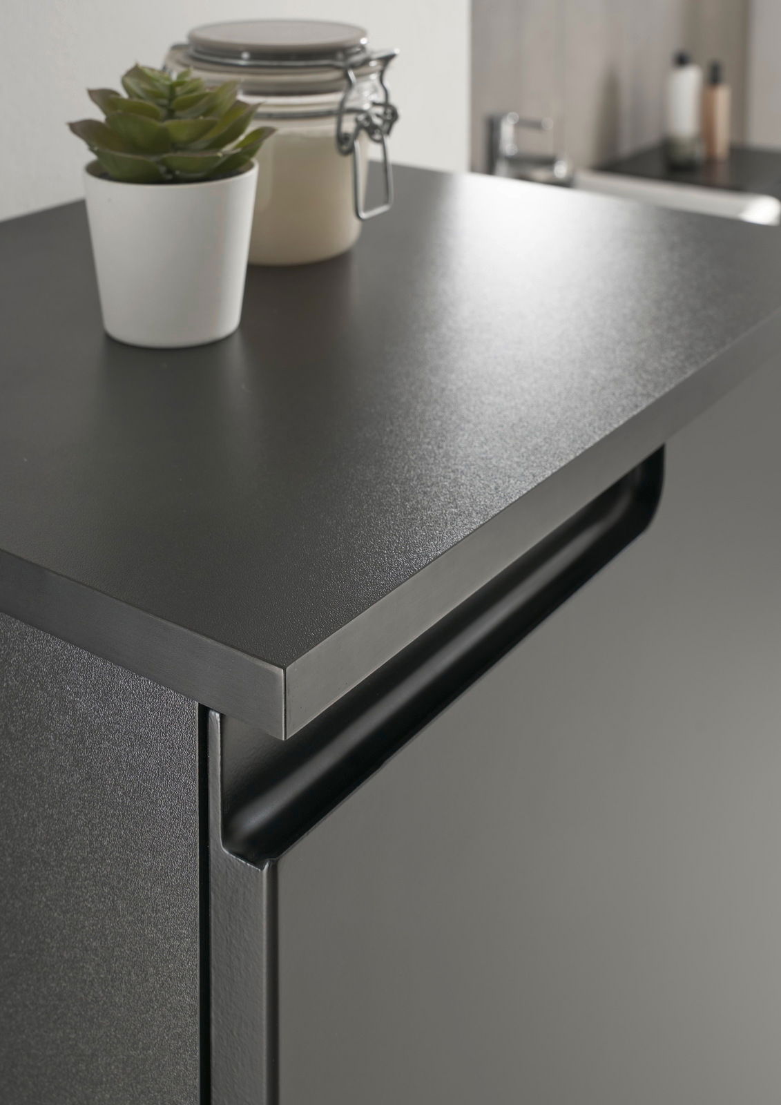 Nahaufnahme eines modernen, schwarzen Highboards mit einer dekorativen Pflanze und einem Glasbehälter auf der Oberseite, seitliche Perspektive.