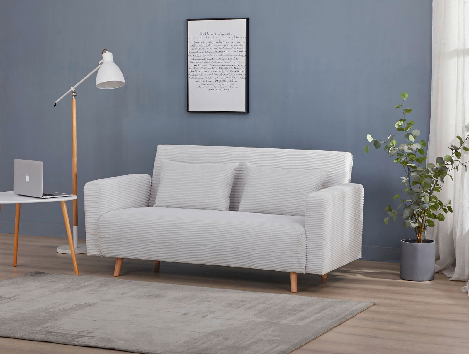 Modernes Funktionssofa in hellem Grau, frontal fotografiert, mit zwei Kissen, neben einem weißen Beistelltisch und einer Stehlampe, vor einer blauen Wand.