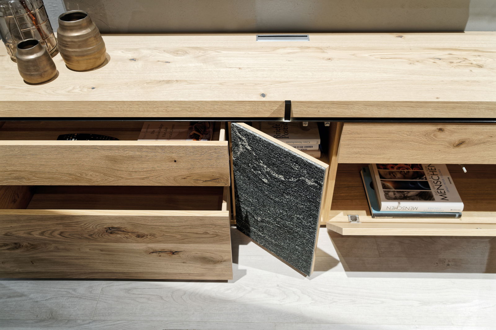 Wohnwand aus hellem Holz mit offenen Schubladen und Fächern, von oben fotografiert.