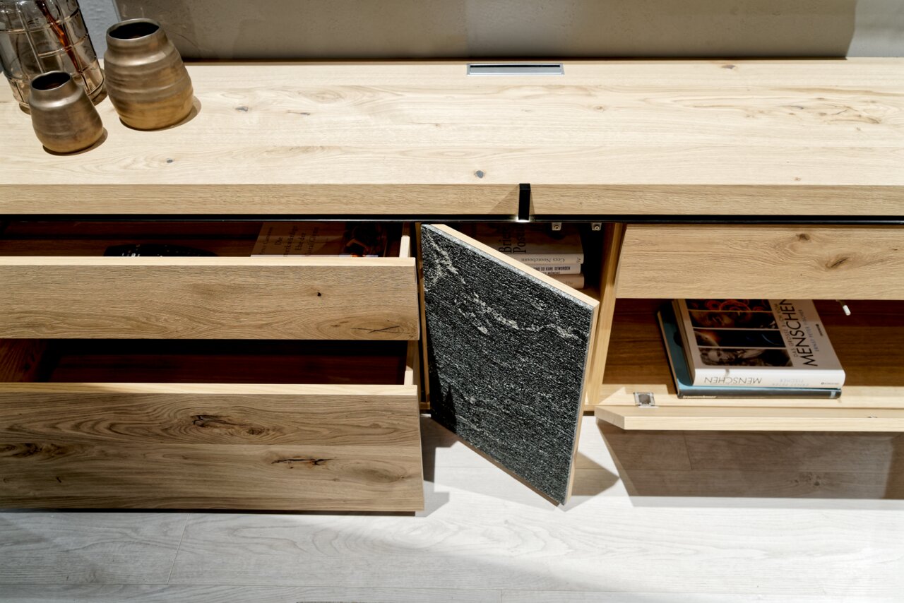 Wohnwand aus hellem Holz mit offenen Schubladen und Fächern, von oben fotografiert.