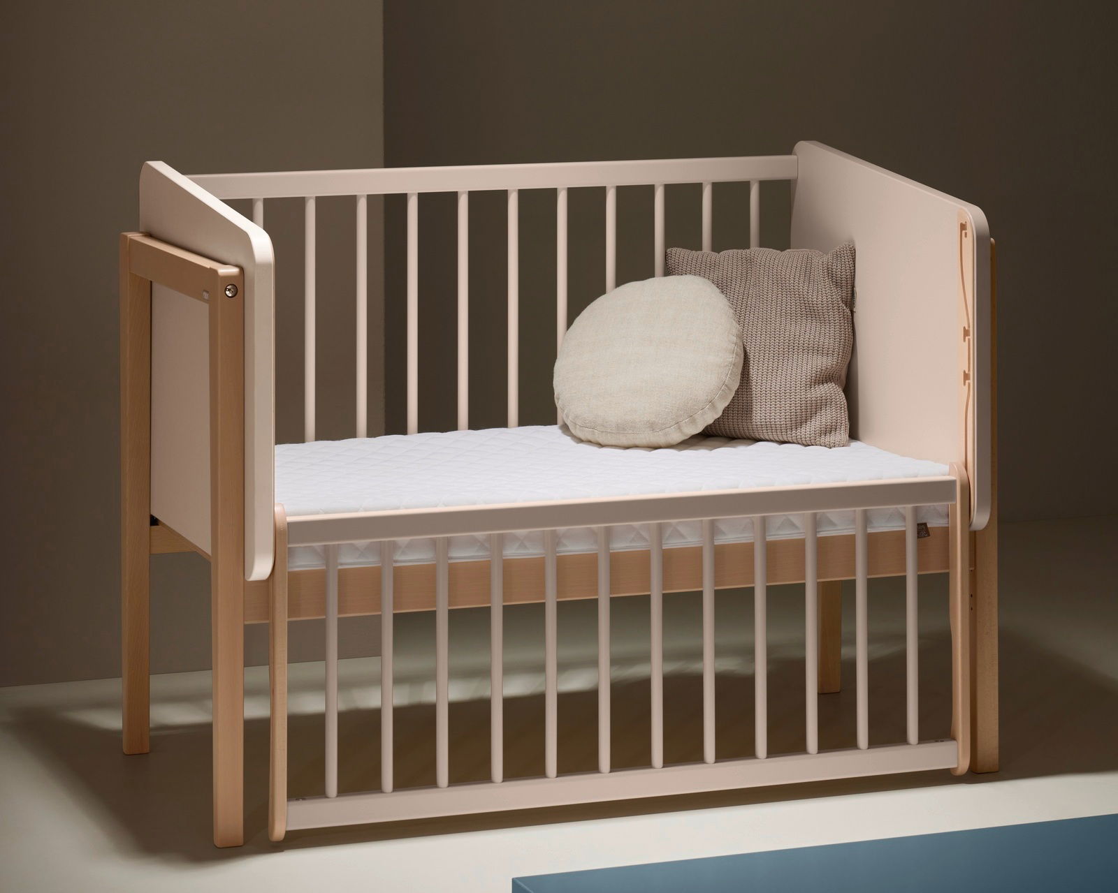 Anstellbett aus Holz mit weißen Gitterstäben, seitliche Perspektive, zwei Kissen auf der Matratze.