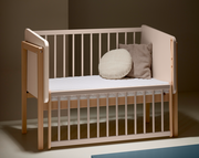 Anstellbett aus Holz mit weißen Gitterstäben, seitliche Perspektive, zwei Kissen auf der Matratze.