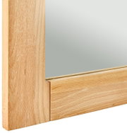 Nahaufnahme eines Spiegels mit einem Rahmen aus hellem Holz, perspektivisch von der Seite aufgenommen.