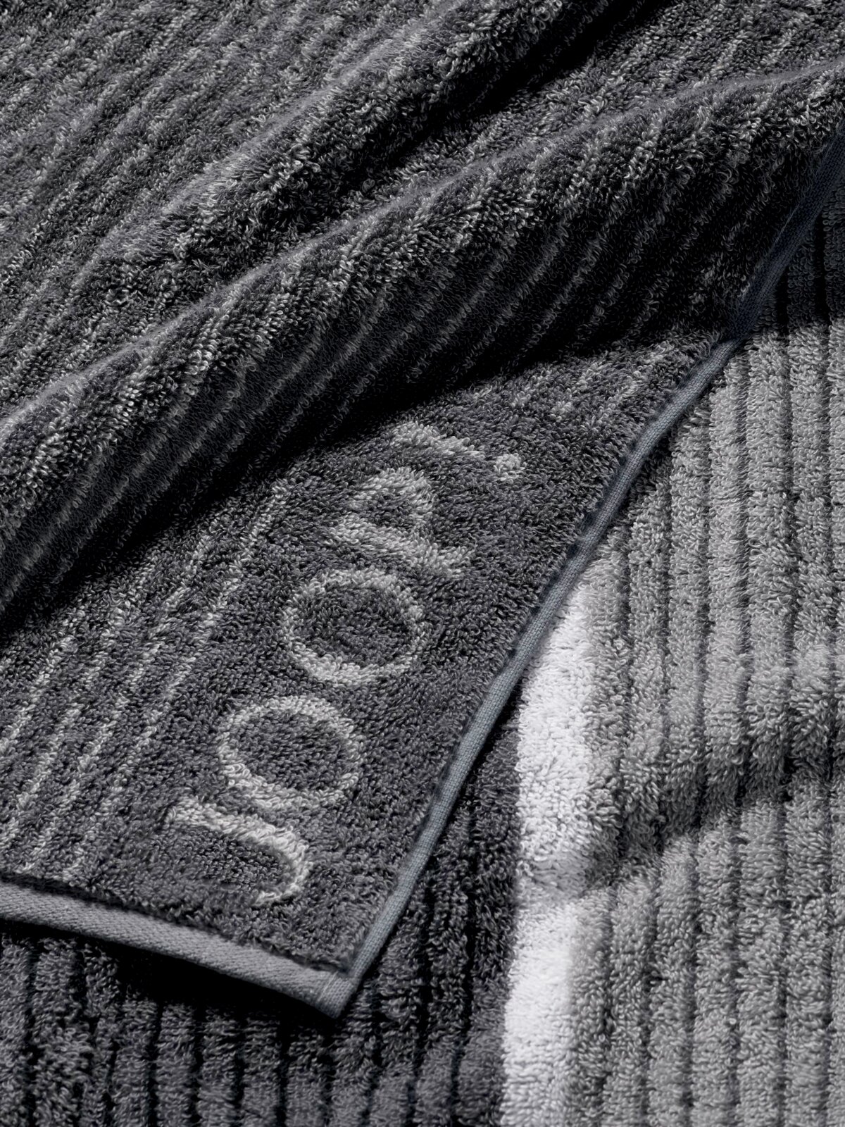 Grijze douchehanddoek met ingeweven logo, close-up van de textuur en de rand.