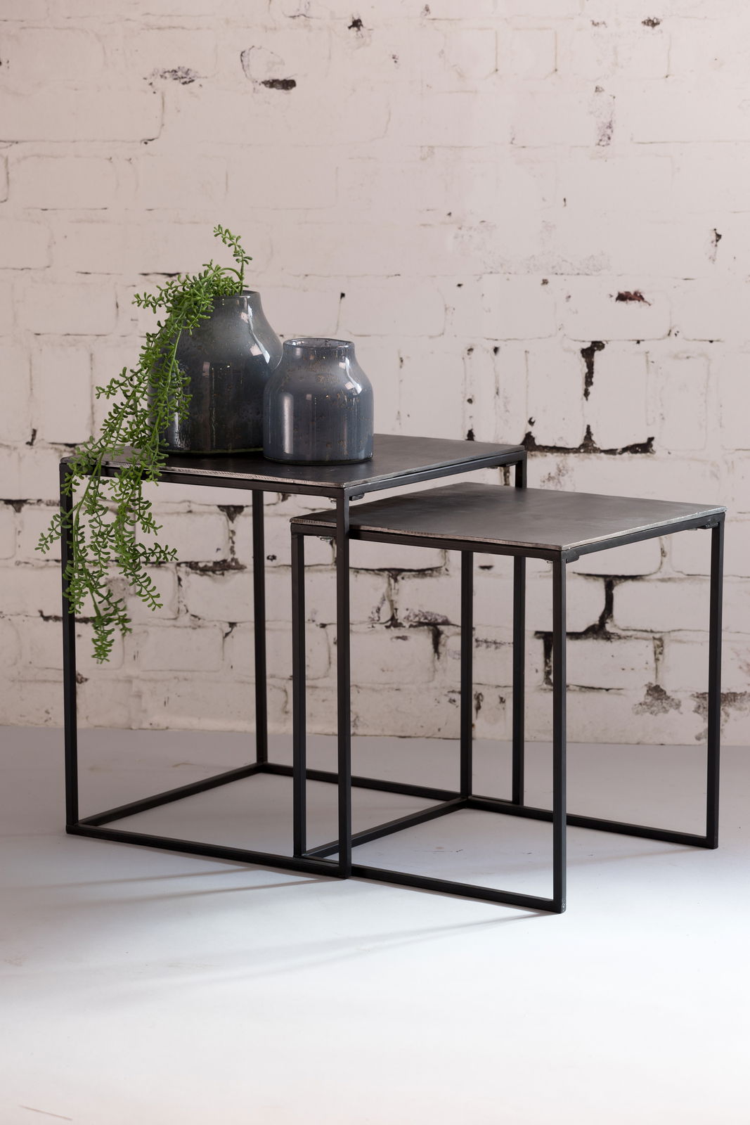 Light&Living Beistelltisch BANOS Zwei ineinander verschachtelte Beistelltische aus Metall mit dunkler Oberfläche, dekoriert mit zwei blauen Vasen und einer hängenden Pflanze, seitliche Perspektive.