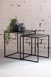 Zwei ineinander verschachtelte Beistelltische aus Metall mit dunkler Oberfläche, dekoriert mit zwei blauen Vasen und einer hängenden Pflanze, seitliche Perspektive.