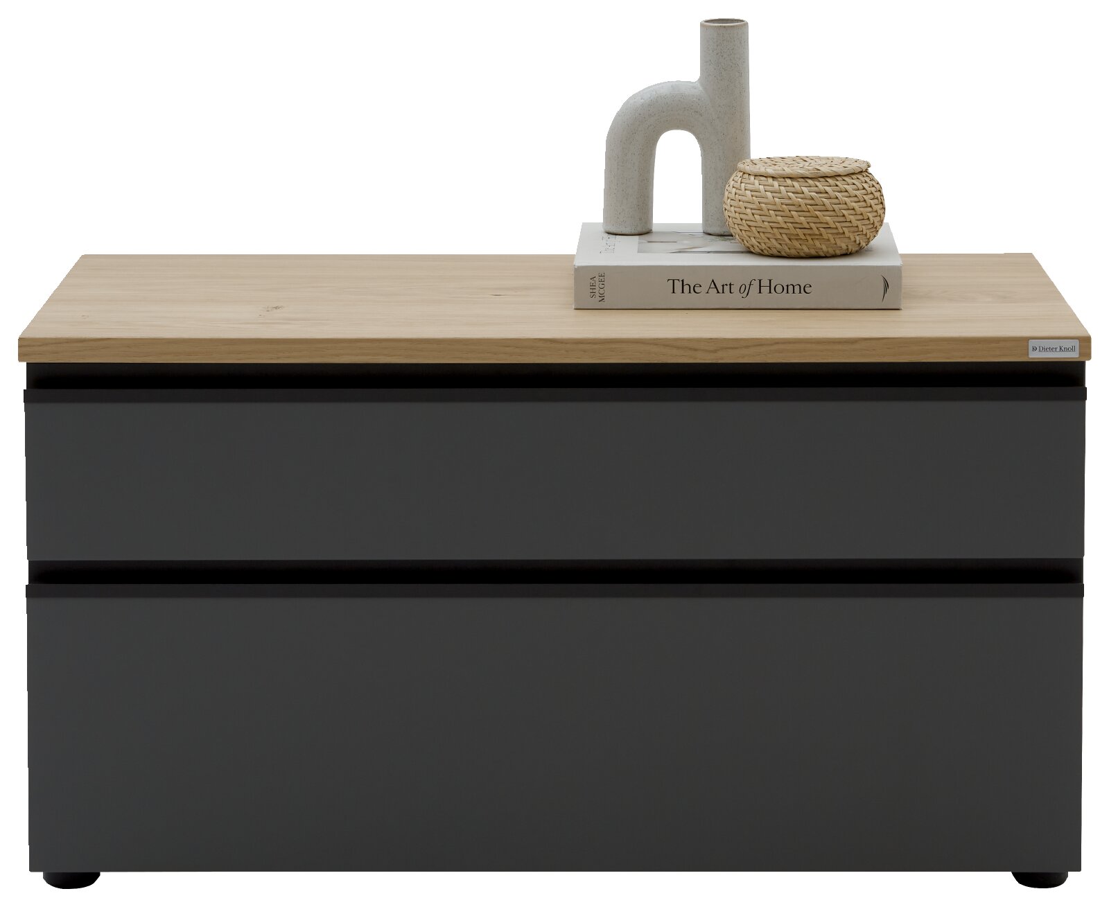 Frontansicht auf eine moderne Kommode mit mattschwarzer Front und heller Holzplatte, oben dekoriert mit Buch, Keramikvase und geflochtenem Korb vor weißem Hintergrund.