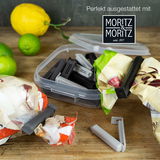 Verschlussclips in einer offenen Plastikbox, umgeben von verpackten Lebensmitteln und Zitrusfrüchten, aus der Vogelperspektive.