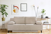 Beige Querschläfer-Sofa in einem modernen Wohnzimmer, frontal fotografiert. Umgeben von Pflanzen, Kunstwerken und einem Beistelltisch.