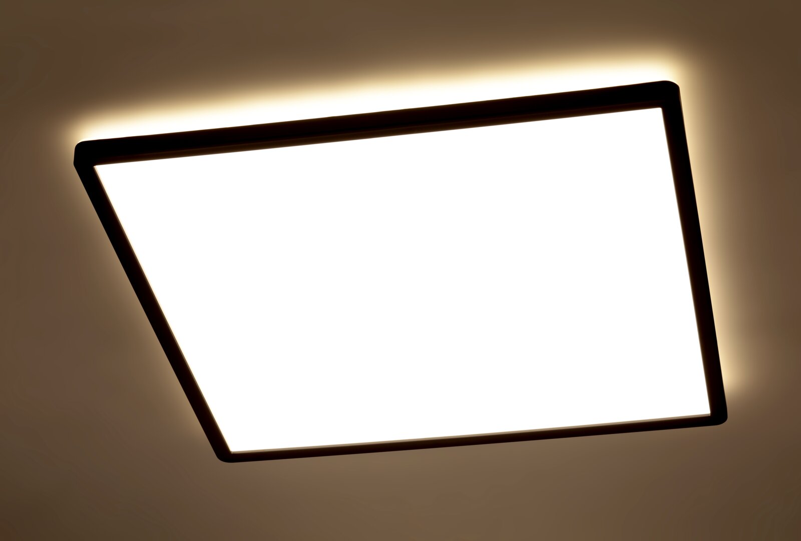 Quadratische LED-Deckenleuchte mit schwarzem Rahmen, von unten betrachtet, mit warmem Lichtschein an der Decke.