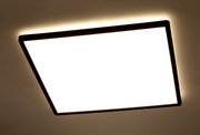 Quadratische LED-Deckenleuchte mit schwarzem Rahmen, von unten betrachtet, mit warmem Lichtschein an der Decke.