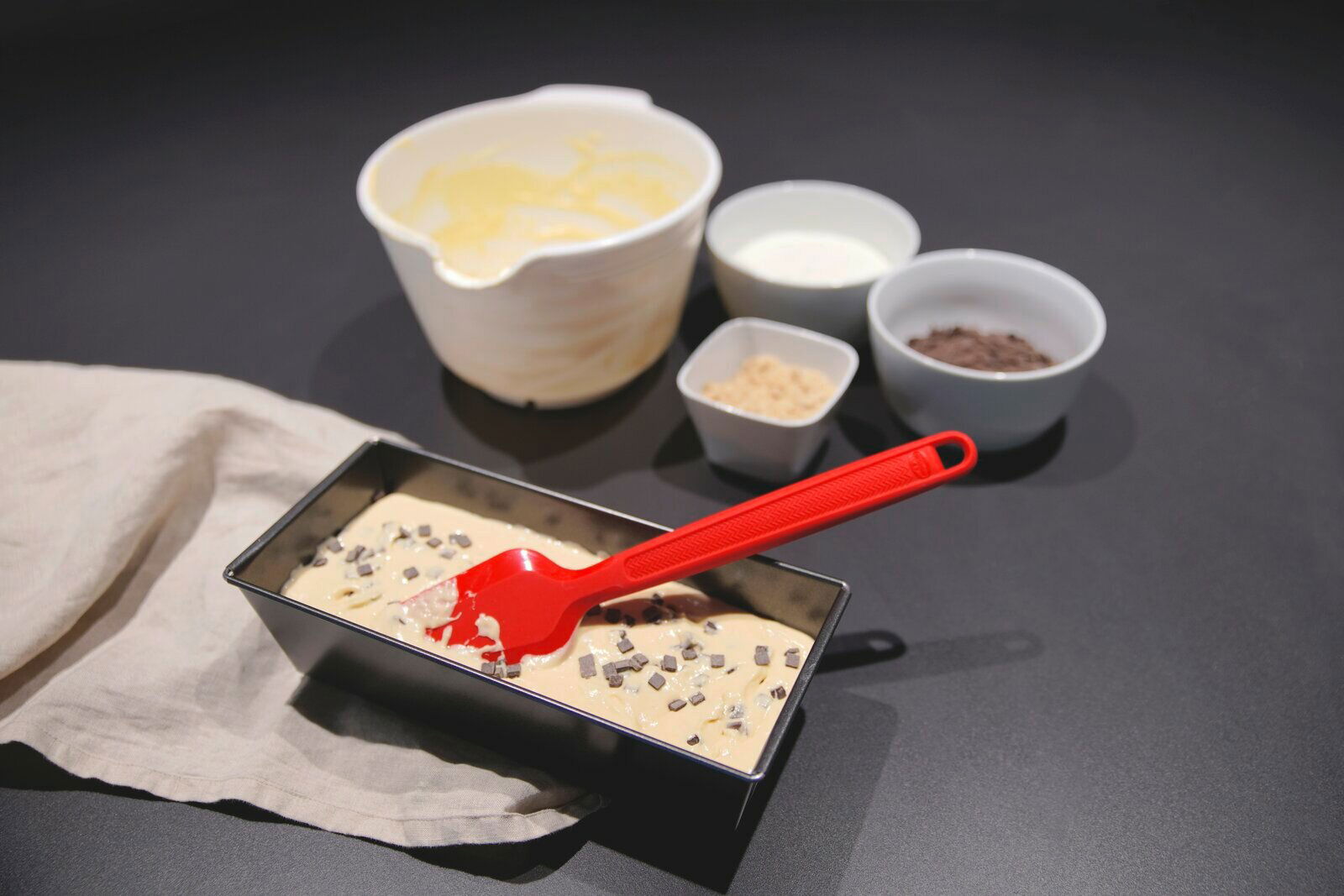 Dr. Oetker Silikon-Teigschaber Roter Silikon-Teigschaber in einer Kastenform mit Teig, umgeben von Schüsseln mit Zutaten, aus der Vogelperspektive.