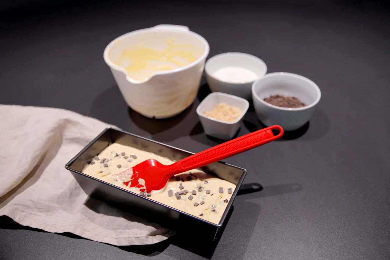 Dr. Oetker Silikon-Teigschaber Roter Silikon-Teigschaber in einer Kastenform mit Teig, umgeben von Schüsseln mit Zutaten, aus der Vogelperspektive.