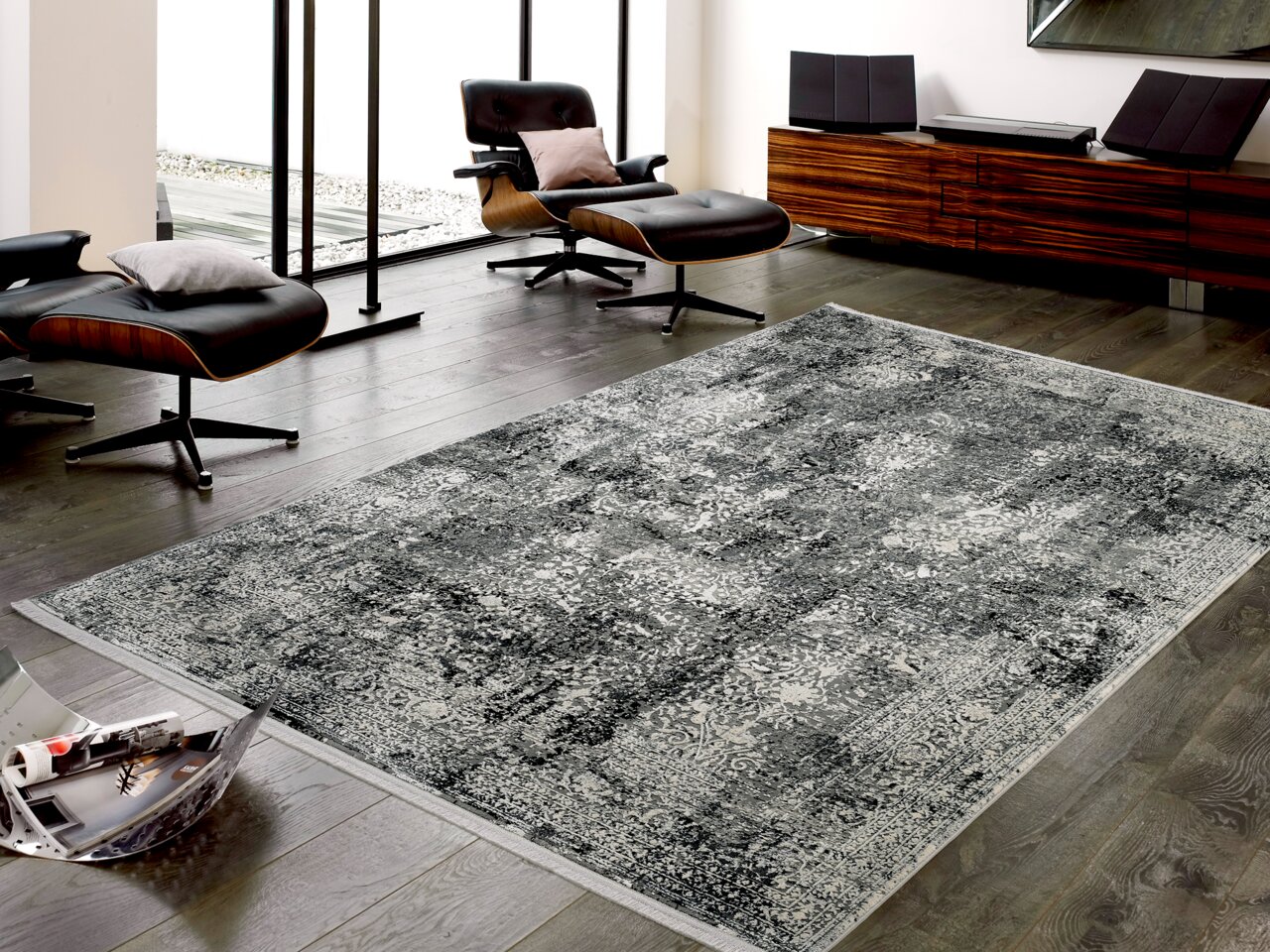 Designer Teppich in einem modernen Wohnzimmer mit dunklem Holzboden, zwei schwarzen Lounge-Stühlen und einem Holz-Sideboard, aus der Perspektive von schräg oben fotografiert.