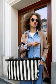 Schwarz-weiß gestreifter Einkaufskorb mit schwarzem Griff, von vorn in leichter Untersicht fotografiert, getragen von einer Frau vor einer Haustür.