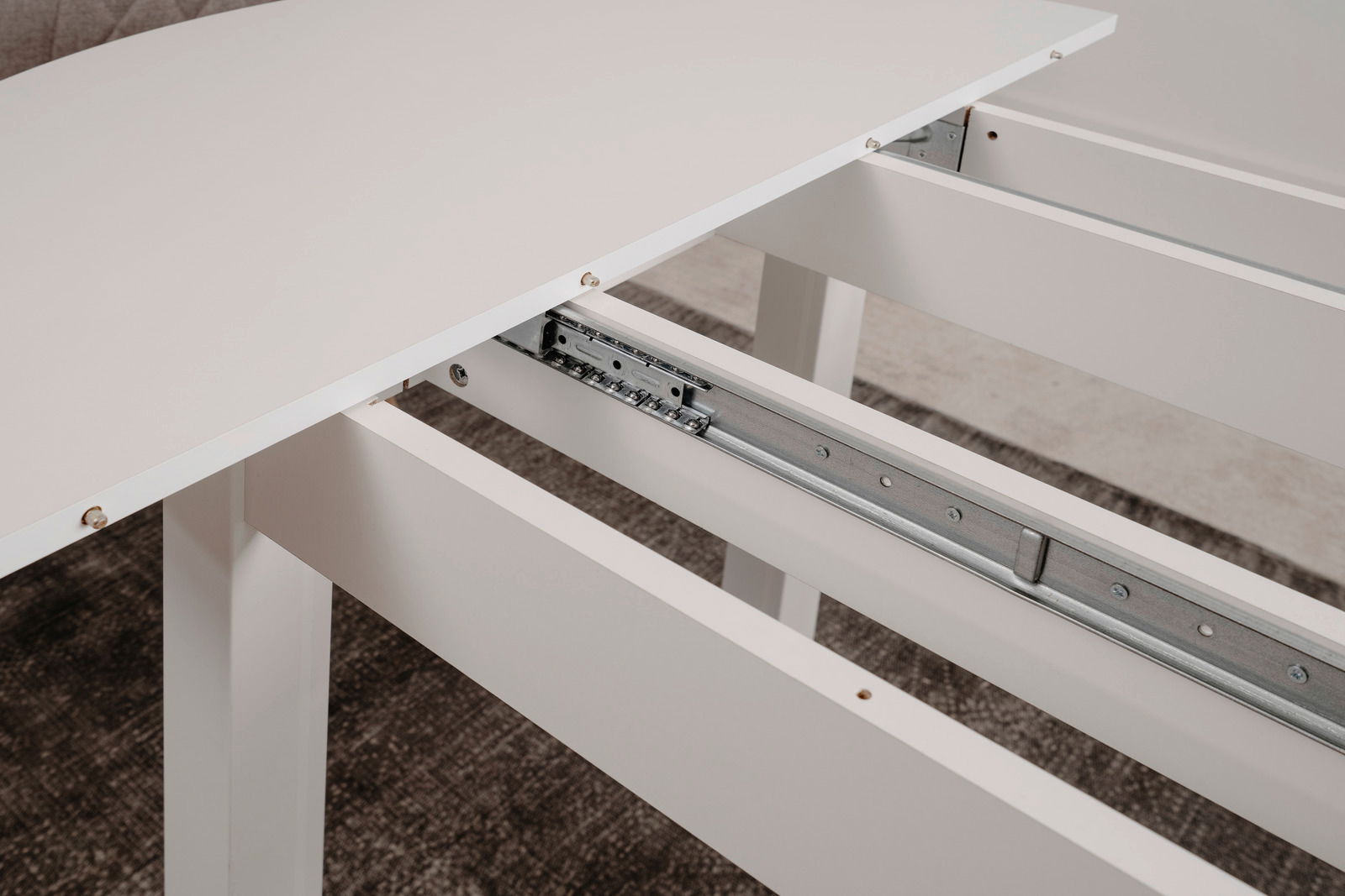 Nahaufnahme eines weißen Esstisches mit ausziehbarer Tischplatte und Metallschienenmechanismus.