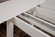Nahaufnahme eines weißen Esstisches mit ausziehbarer Tischplatte und Metallschienenmechanismus.