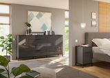 Modernes Schlafzimmer mit einem großen, glänzenden Sideboard und einer passenden Nachtkommode in dunklem Design, seitliche Perspektive.