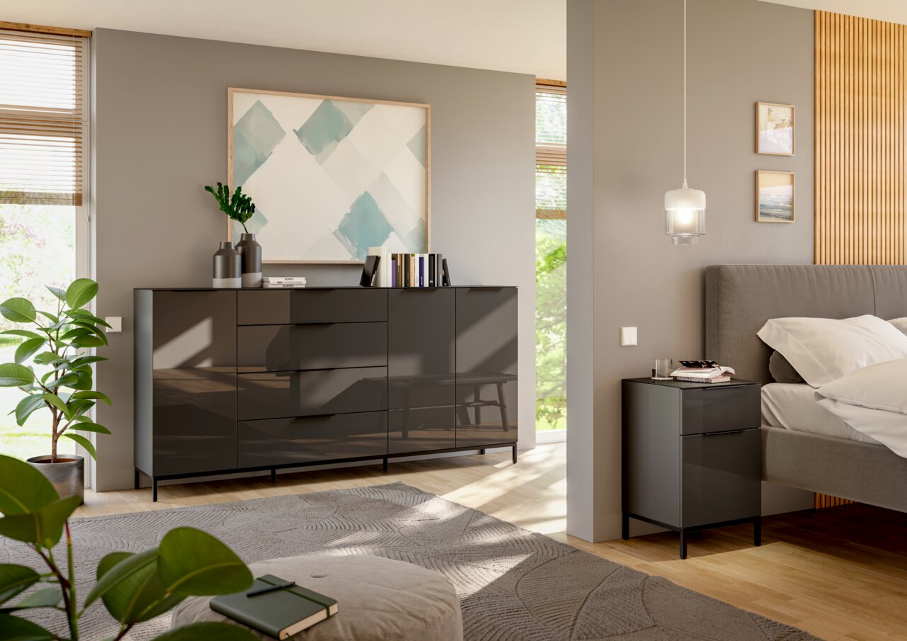 Novel XXL-Sideboard STYLE Modernes Schlafzimmer mit einem großen, glänzenden Sideboard und einer passenden Nachtkommode in dunklem Design, seitliche Perspektive.