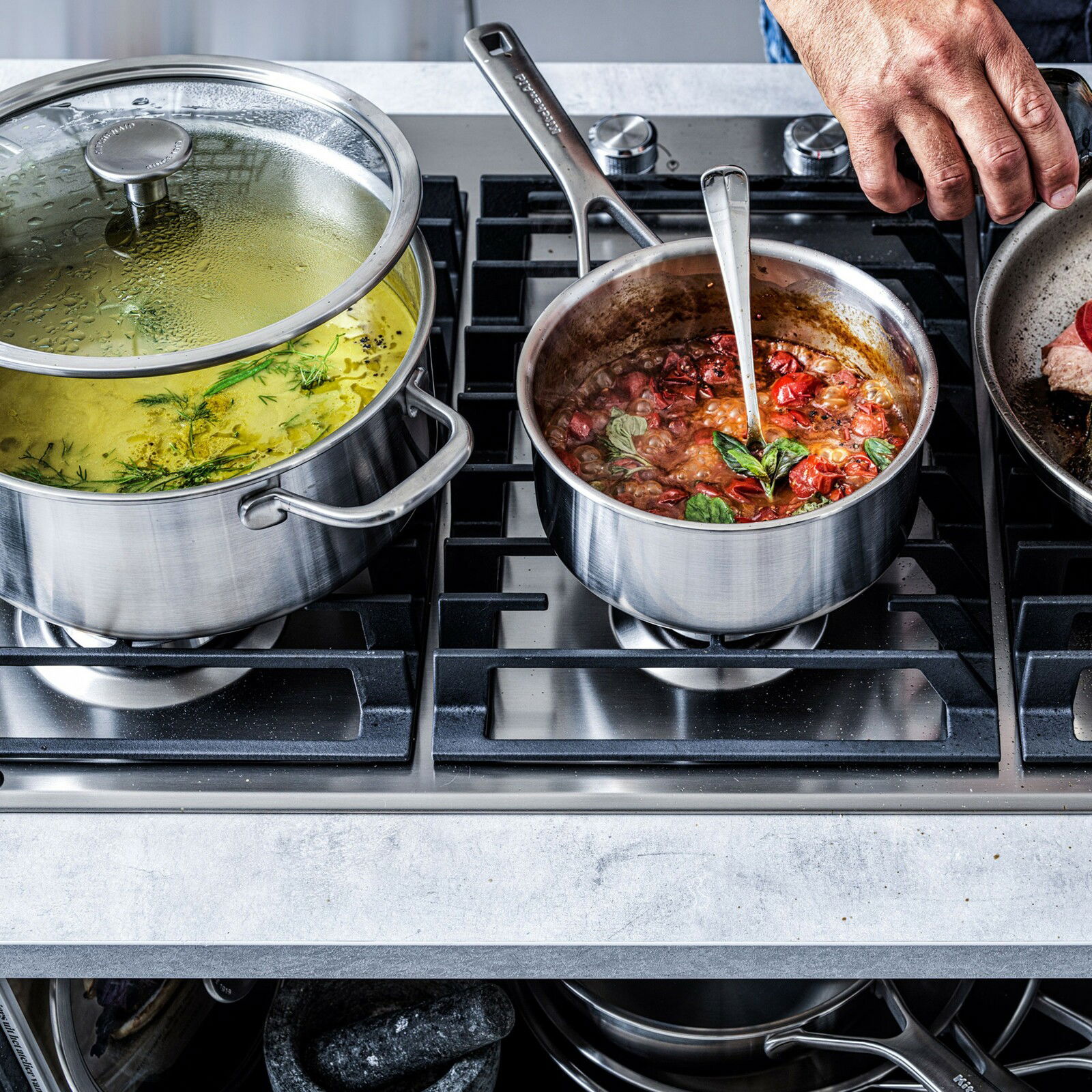 KitchenAid Topfset 4-tlg. Topfset aus Edelstahl auf einem Herd, gefüllt mit kochenden Speisen, aus der Vogelperspektive fotografiert.